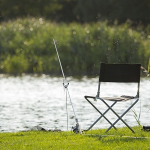 Coarse fishing tackle on the banks of a lake with sun glinting on the water in the background