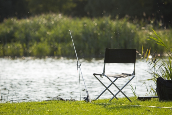 Coarse fishing tackle on the banks of a lake with sun glinting on the water in the background