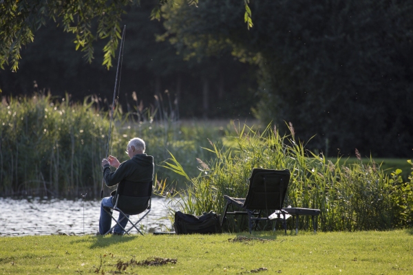 A coarse fisherman or angler adjusting his float fishing gear on the river bank with sunlit water in the background