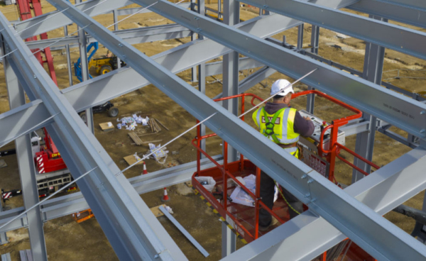 A steelworker on a lift platform on a large construction site