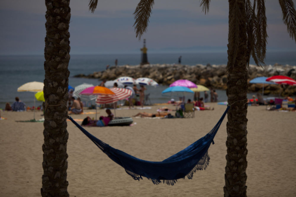 Holiday hammock strung between two palm trees on the beach at Portofino, Marbella in Southern Spain on the Costa del Sol