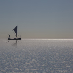 a silhouette of a thames sailing barge on a sunlit horizon