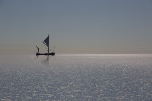 a silhouette of a thames sailing barge on a sunlit horizon